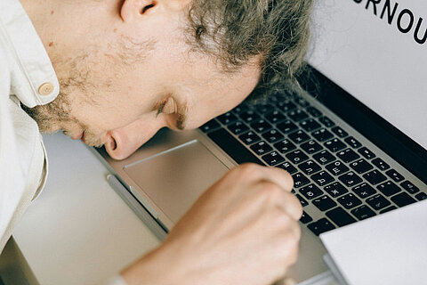 Person sitzt kraftlos vor dem Laptop und wirkt emotional erschöpft.